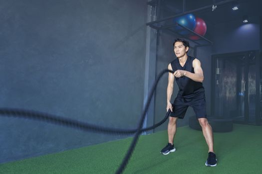 Man wearing a tank top to exercise at the gym with battle ropes during his fitness workout. High-Intensity Interval Training.