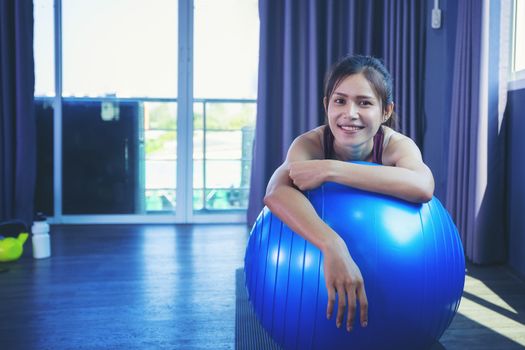 Beautiful woman is exercising by playing Pilates ball happily in a public gym.