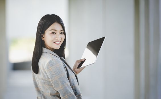 Portrait of business woman looking digital tablet with white travel bag on walkway while waiting to travel to the destination 