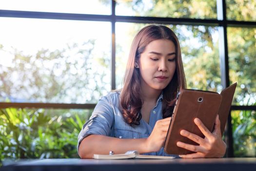 Beautiful Asian businesswoman who uses a tablet in the coffee shop to contact customers and check emails. Business concept