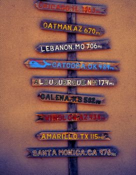 Wooden pole pointing the distance in miles to different cities through Route 66 from Chicago to Los angeles.