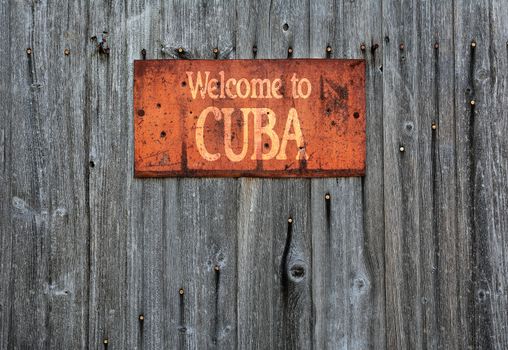 Rusty metal sign on wooden wall with the phrase: Welcome to Cuba.