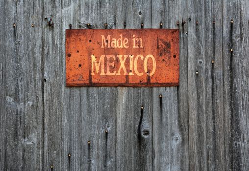 Rusty metal sign on wooden wall with the phrase: Made in Mexico.