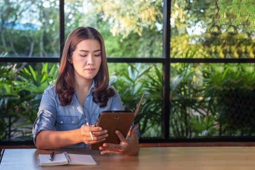 Beautiful Asian businesswoman who uses a tablet in the coffee shop to contact customers and check emails. Business concept