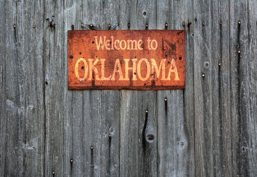 Rusty metal sign on wooden wall with the phrase: Welcome to Oklahoma.