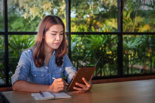 Beautiful Asian businesswoman who uses a tablet in the coffee shop to contact customers and check emails. Business concept