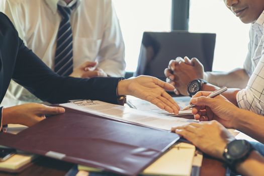 Businessmen negotiate and sign contracts. They are pointing to documents and discussing businessmen and customers. DEAL agreement Working together, talking in the office concept.