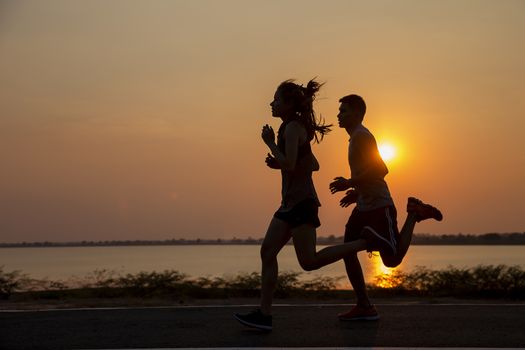 Lovers on the rural road at sunset in summer field. silhouette, running sportsman in the sun, toning. Lifestyle sports background 
