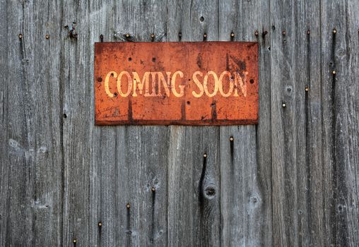 Rusty metal sign on wooden wall with the phrase: Coming soon.