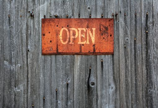 Rusty metal sign on wooden wall with the word Open.