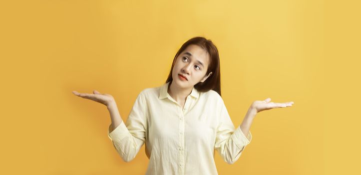 Beautiful Asian women showing open two hand palm and looking sideway on yellow background with copy space.