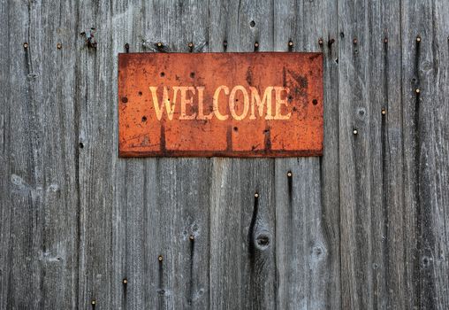 Rusty metal sign on wooden wall with the word Welcome.