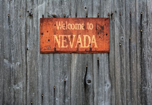 Rusty metal sign on wooden wall with the phrase: Welcome to Nevada.