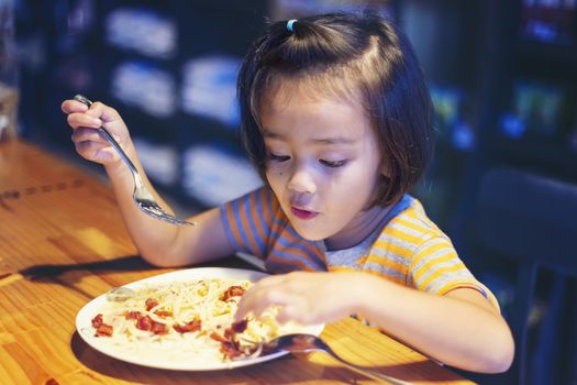 Asian little girl is eating spaghetti bolognese in the restaurant happily.