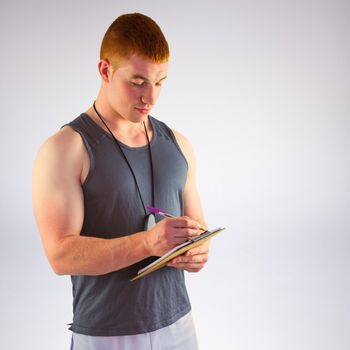 Fit personal trainer writing on clipboard against grey background
