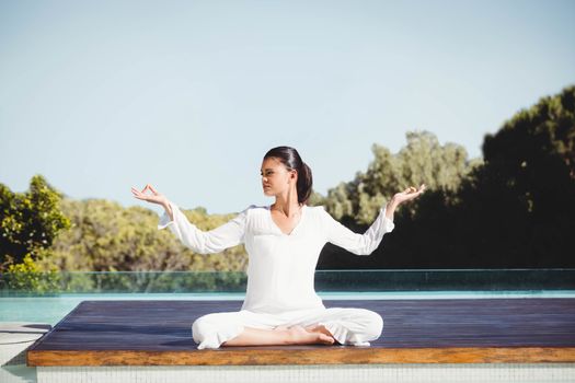 Calm brunette doing yoga by the pool