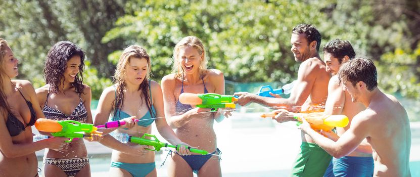 Happy friends doing water gun battle poolside