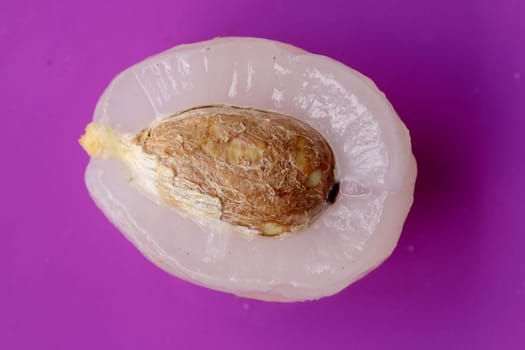 Close up of peeled fruit Rambutan on purple background. Top view of one healthy fruit. Ready to Eat Sweet Bali Fruit. Half fruit with stone in the middle of the fruit.