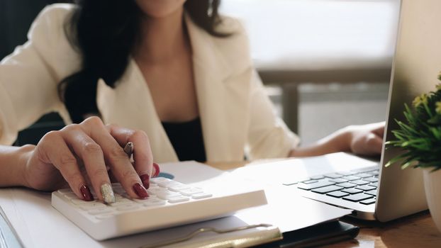 Close up Business woman using calculator and laptop for do math finance on wooden desk in office and business working background, tax, accounting, statistics and analytic research concept
