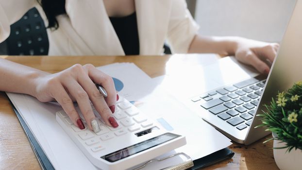 Close up Businesswoman using calculator and laptop for do math finance on wooden desk in office and business working background, tax, accounting, statistics and analytic research concept
