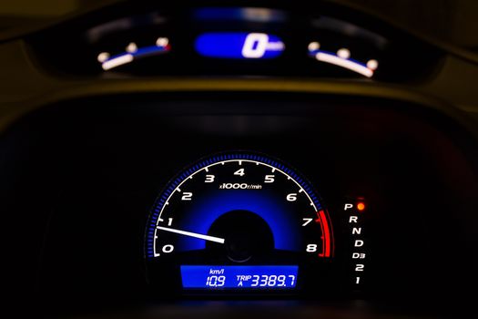 Car dashboard displaying illuminated speedometer and tachometer in HDR.