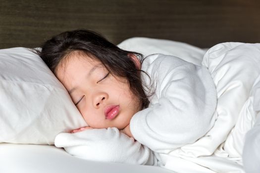 Little girl sleeping in bed with white blanket.