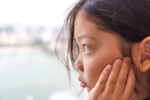 Sad little girl looking out of window waiting for someone.
