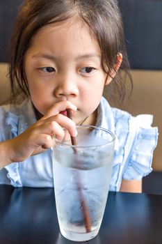 Asian Child drinking water from glass using straw.