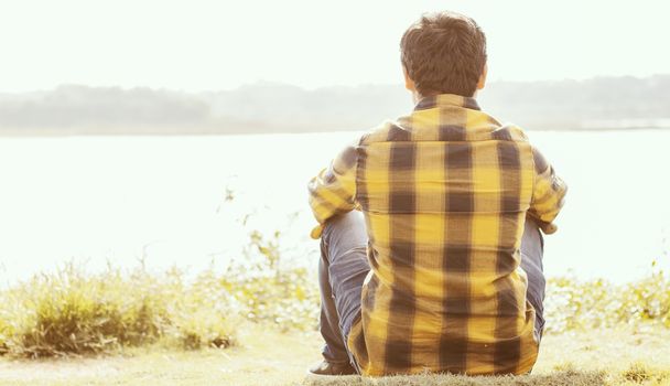 A lonely man sitting in front of the lake In sunny day - Concept of loneliness, break up,single and alone