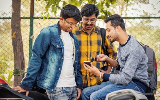Students busy on mobile at college parking area on bike - Young millennials busy on phones and technology - concept of friendship and urban youthful lifestyle