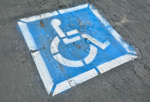 Disabled blue parking sign painted on dark asphalt.