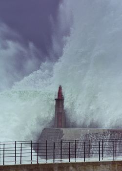 Stormy wave over old lighthouse and pier of Viavelez in Asturias, Spain.