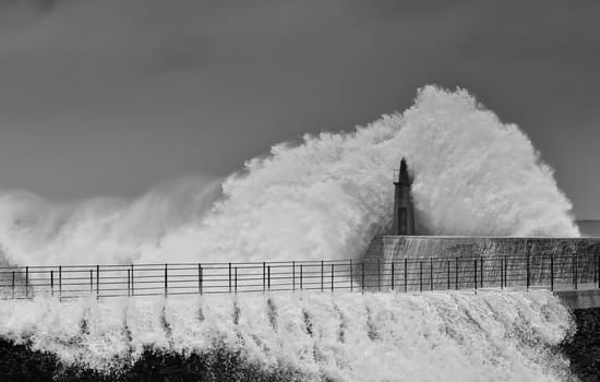 Stormy wave over old lighthouse and pier of Viavelez in Asturias, Spain.