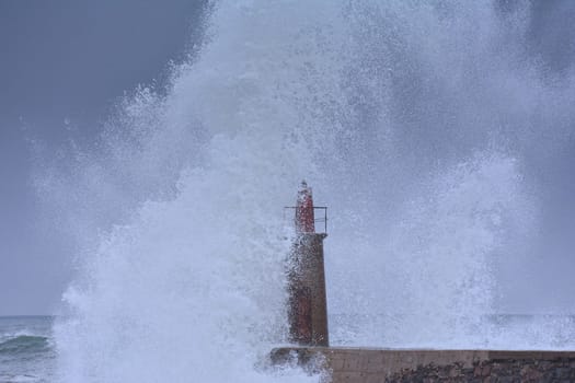 Stormy wave over old lighthouse and pier of Viavelez in Asturias, Spain.