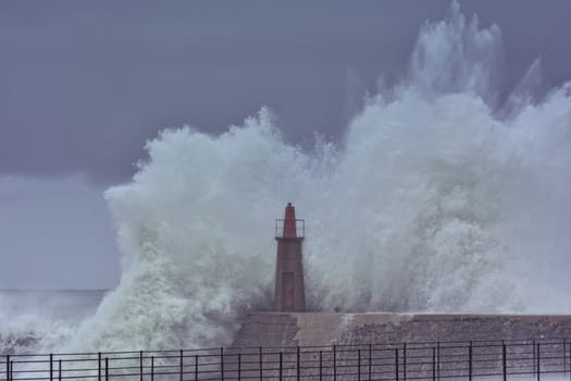 Stormy wave over old lighthouse and pier of Viavelez in Asturias, Spain.