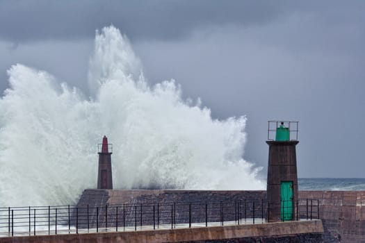 Stormy wave over old lighthouse and pier of Viavelez in Asturias, Spain.