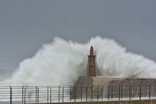 Stormy wave over old lighthouse and pier of Viavelez in Asturias, Spain.