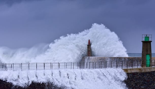 Stormy wave over old lighthouse and pier of Viavelez in Asturias, Spain.