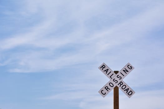 Railroad crossing sign against blue sky background, with space for your text.