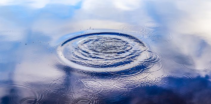 Beautiful water at a lake with splashing water and ripples on the surface with clouds and sky reflections