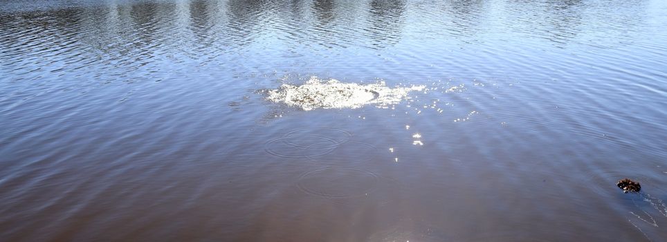 Beautiful water at a lake with splashing water and ripples on the surface with clouds and sky reflections