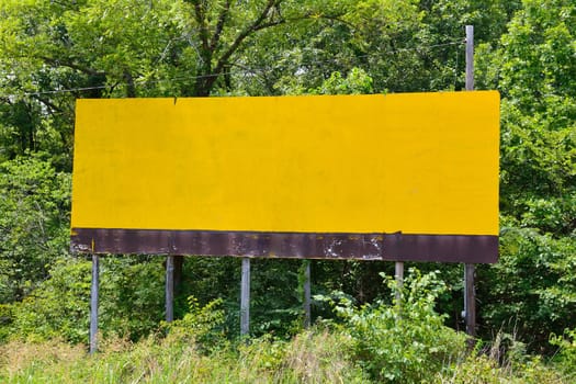 Empty large yellow advertising billboard in green background.