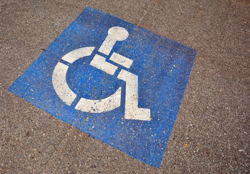 Disabled blue parking sign painted on dark asphalt.