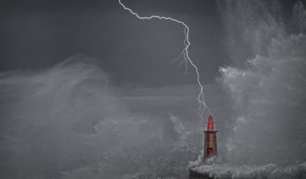 Lightning and wave over old lighthouse and pier of Viavelez in Asturias, Spain.