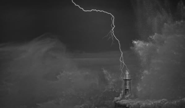 Lightning and wave over old lighthouse and pier of Viavelez in Asturias, Spain.