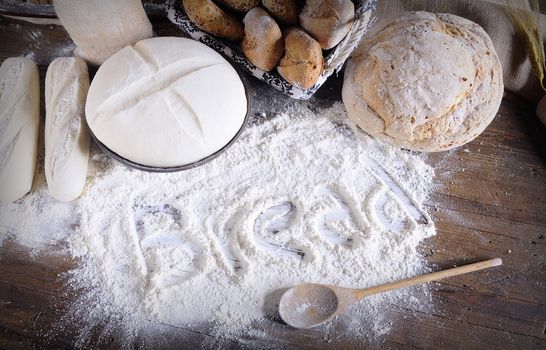 Word 'bread' written on flour scattered on wooden table. Bread making ingredients. From above