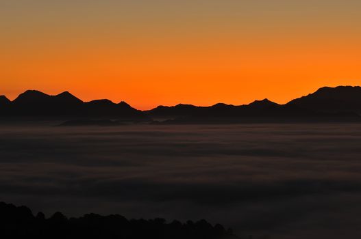 Silhouette of mountains with fog at sunset against of bright vivid sky