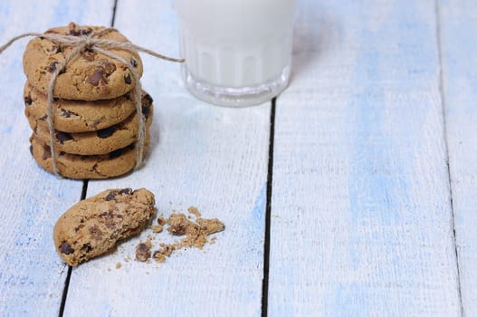 Stack of chocolate chip cookies with glass of fresh milk on blue wooden table