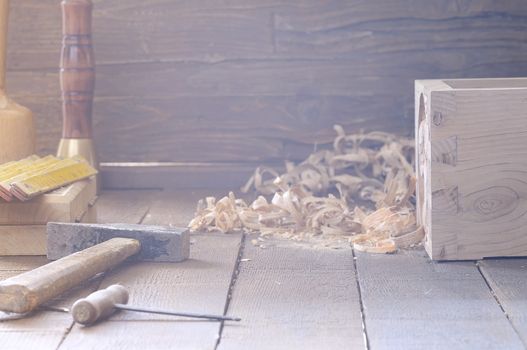 View on hammer, awl, wooden box and chips on wooden floor in daylight