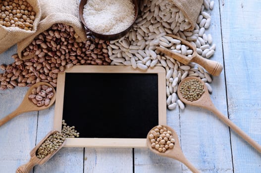 Different cereals on blue wooden table, black board in frame